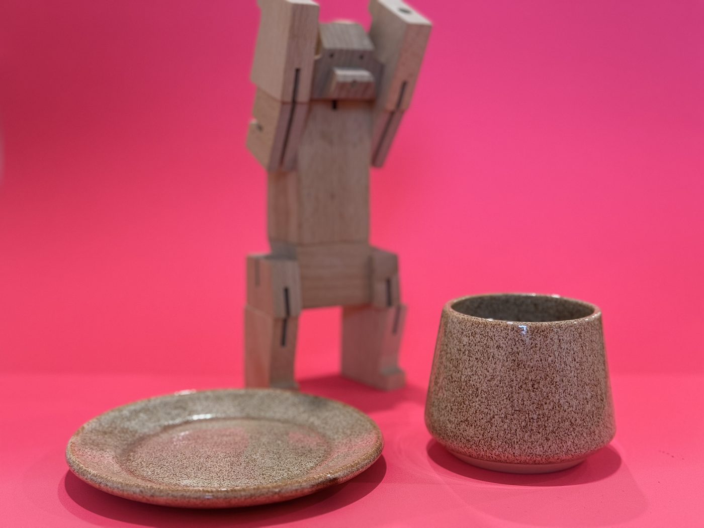 Speckled cup and saucer beside a wooden toy on a pink backdrop